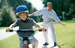 Boy cycling with his father standing behind him